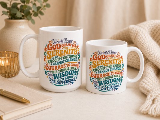 Two white ceramic mugs with colorful spiritual typography, styled on a tabletop with a candle, notebook, pen, and knitted blanket in a warm indoor setting.