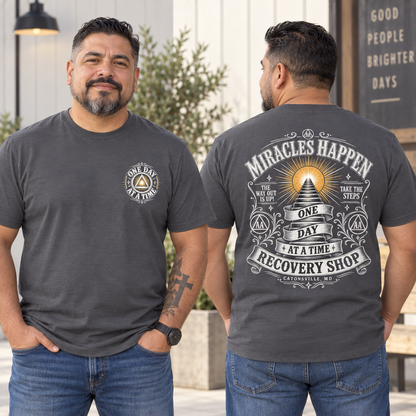 Two views of a man wearing a dark gray graphic t-shirt in an outdoor setting. The left view shows the front of the shirt with a circular 'One Day Recovery' logo on the left chest.